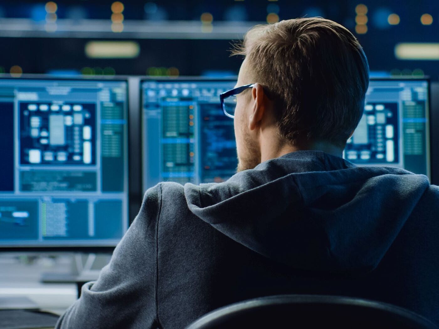 IT-Sicherheitstest Ein Mann sitzt vor drei Computermonitoren mit Code