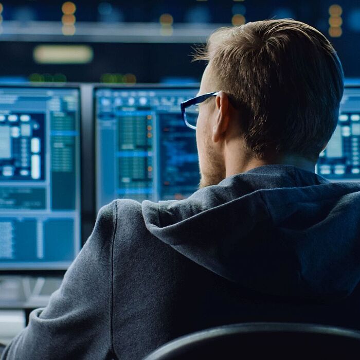 Ein Mann sitzt vor drei Computermonitoren mit Code