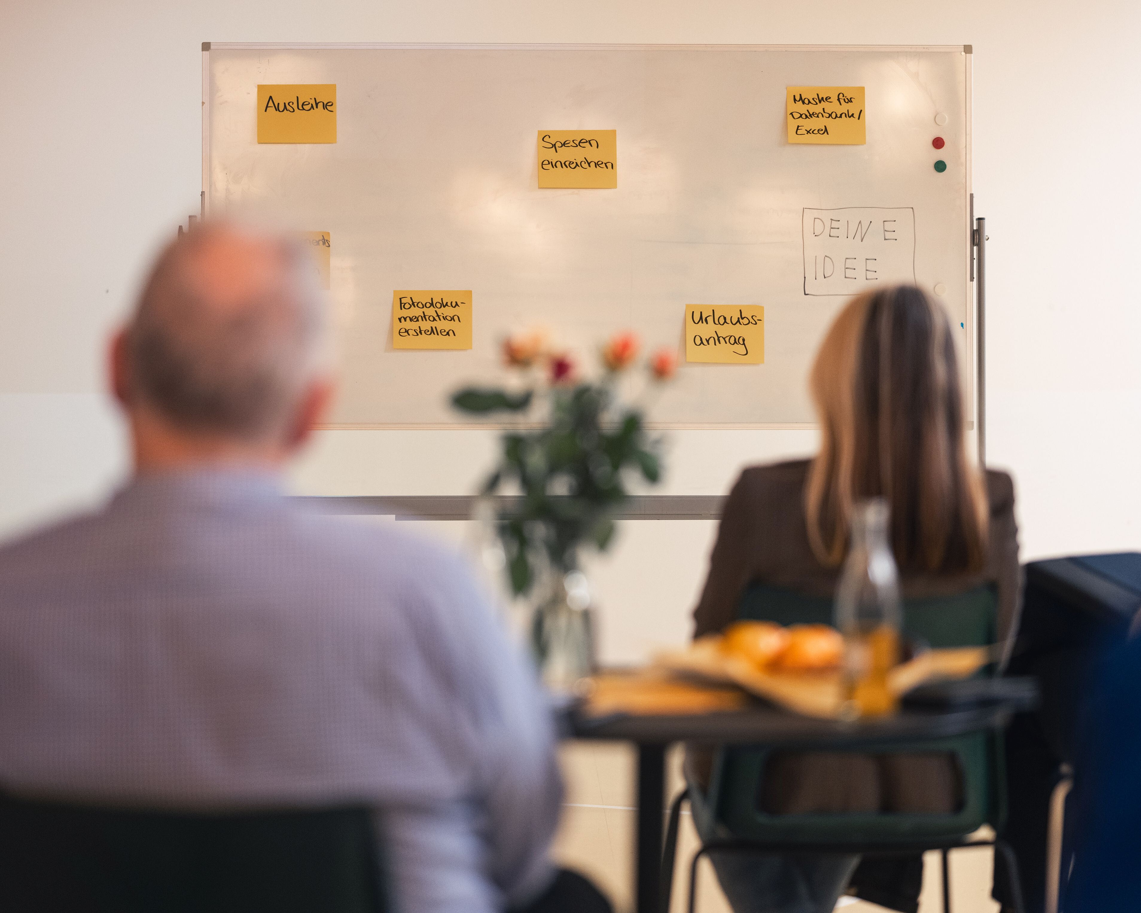 Zwei Personen sitzen vor einem Whiteboard.