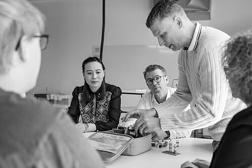 Mehrere Personen am Tisch im Workshopraum gestikulieren und lachen. 