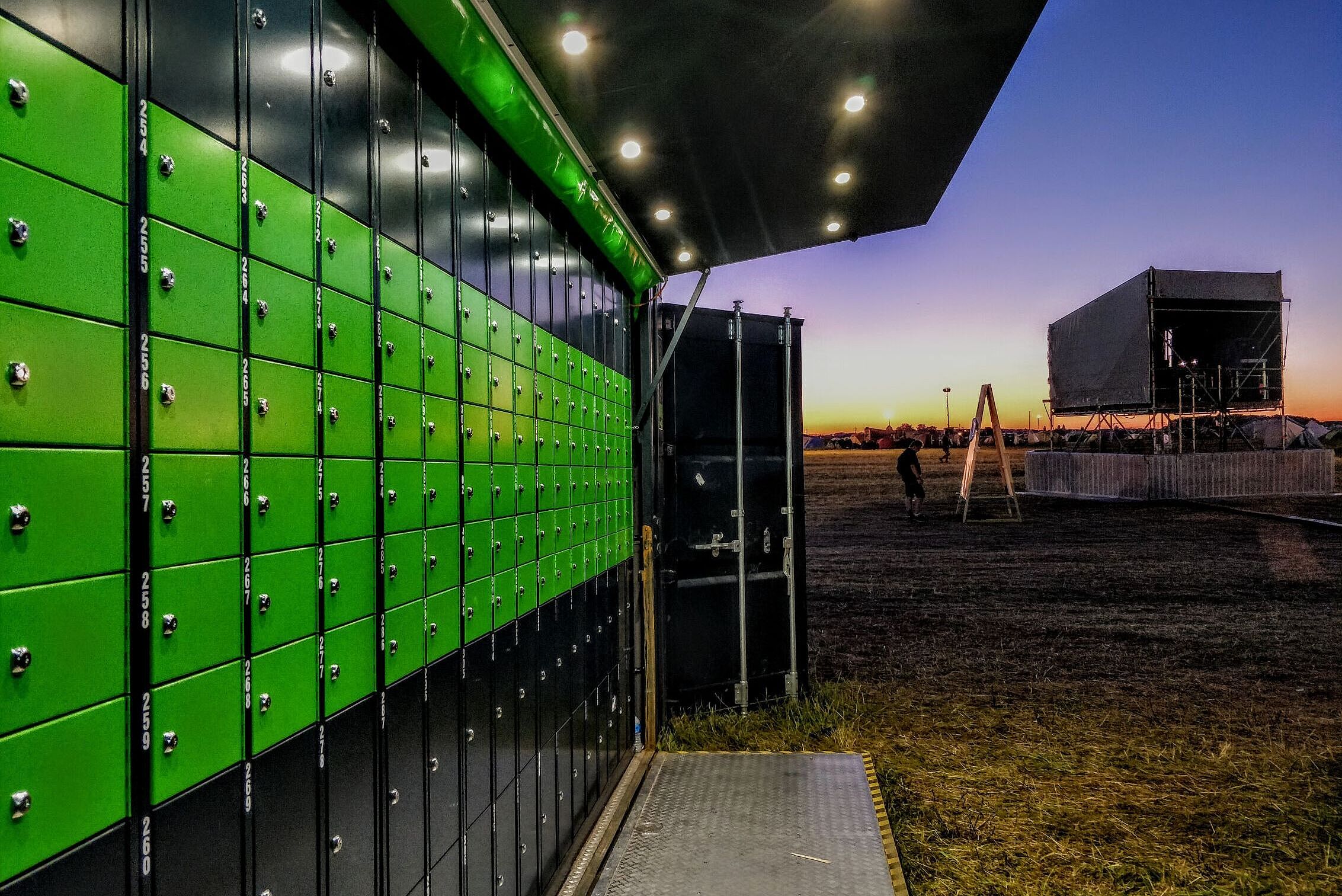 Ein Container mit grünen Schließfächern steht bei Nacht auf einem Festivalgelände Ein Container mit grünen Schließfächern steht bei Nacht auf einem Festivalgelände