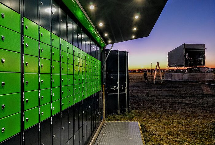 Ein Container mit grünen Schließfächern steht bei Nacht auf einem Festivalgelände