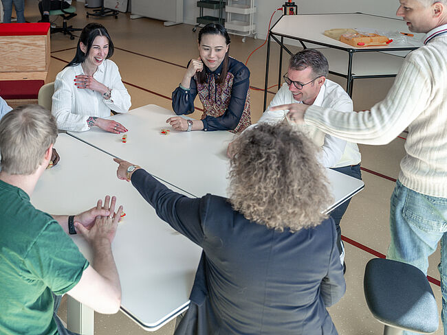 Mehrere Menschen sitzen um einen Tisch in einem Workshopraum im Bürogebäude Schuppen Eins und reden miteinander.