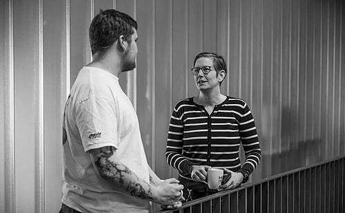 Ein Mann und eine Frau stehen sich auf der Galerie im Foyer der HEC gegenüber und sprechen miteinander.