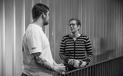 Ein Mann und eine Frau stehen sich auf der Galerie im Foyer der HEC gegenüber und sprechen miteinander.