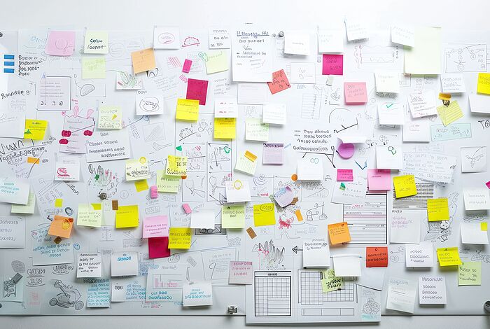 Auf eine Wand sind verschiedene Zettel und Zeichnungen chaotisch durcheinander geheftet.