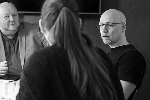 Drei Personen im Gespräch an einem Tisch sitzend.