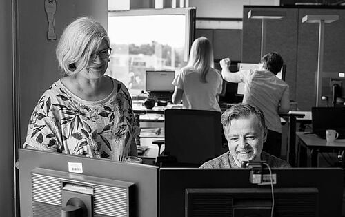 Ein Mann und eine Frau arbeiten gemeinsam vor zwei Monitoren an einem Laptop am Schreibtisch im Büro