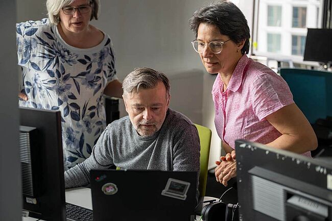 Drei Personen betrachten und besprechen den Inhalt eines Laptopmonitors im Büro.