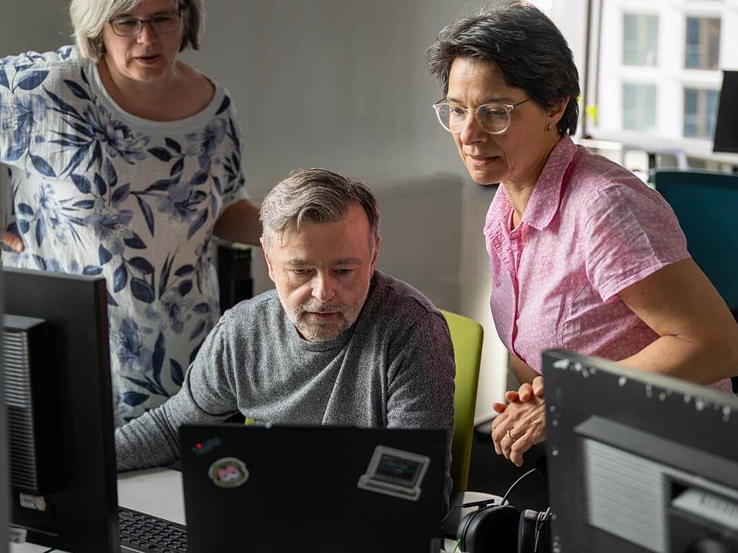 Drei Personen betrachten und besprechen den Inhalt eines Laptopmonitors im Büro.