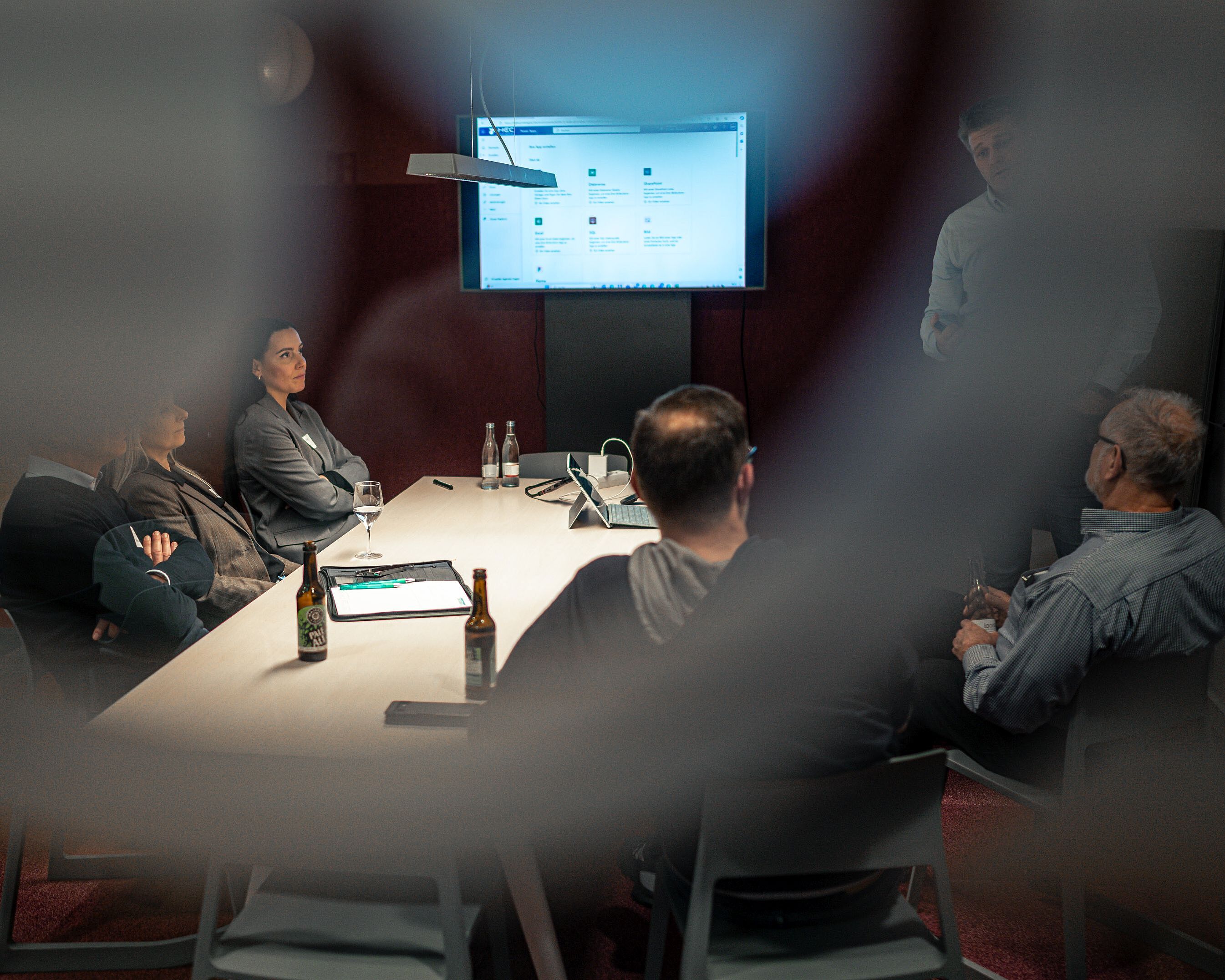 Durch eine Fensterscheibe sind Menschen an einem Schreibtisch zu sehen.