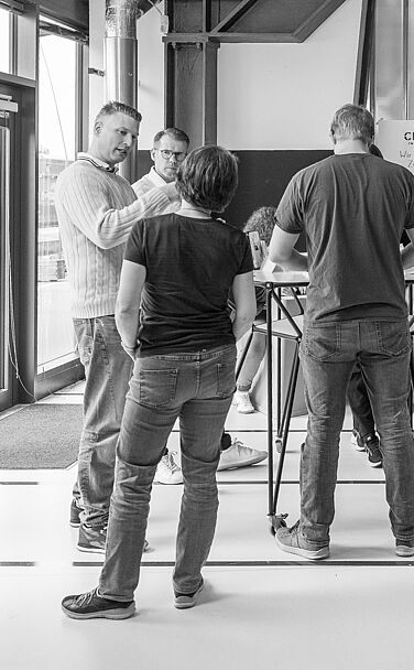 Mehrere Menschen stehen in der Nähe der Terrassentüren in einem Raum und diskutieren