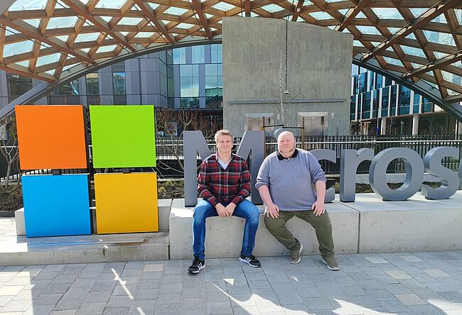 Zwei Männer sitzen vor dem Microsoft-Logo