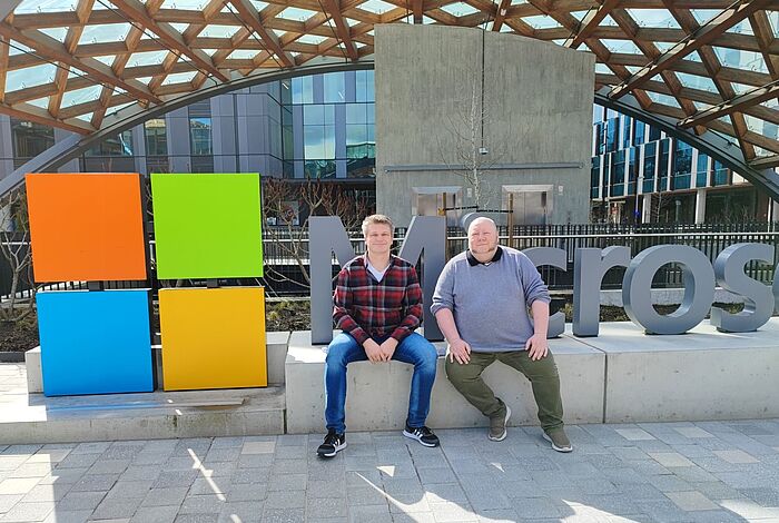 Zwei Männer sitzen vor dem Microsoft-Logo