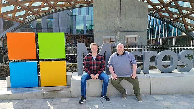 Zwei Männer sitzen vor dem Microsoft-Logo
