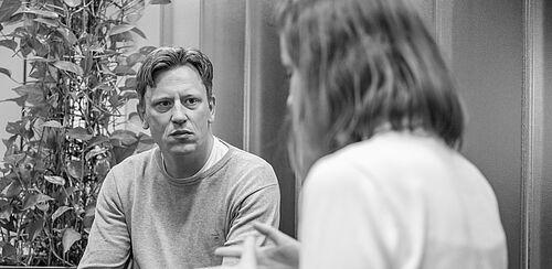 Ein Mann und eine Frau sitzen im Foyer der HEC und sprechen angeregt miteinander.