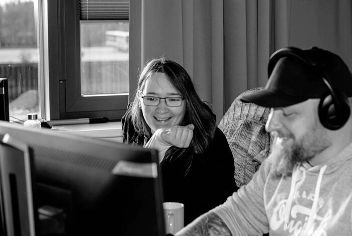 Eine Frau und ein Mann sitzen am PC, er Trägt Kopfhörer