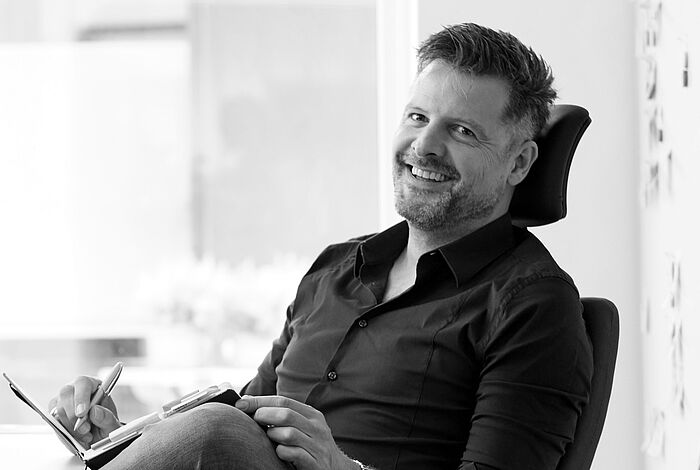 Ein Mann sitzt am Schreibtisch, lacht