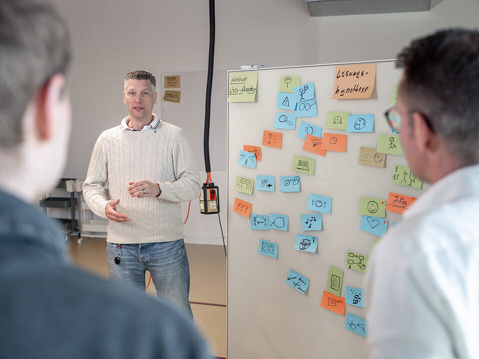 KI Workshop Ein Mann steht neben einer Pinnwand mit viele Klebezetteln und erklärt etwas.
