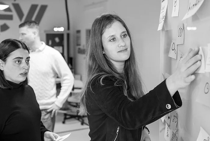 Zwei Frauen kleben Haftnotizen an ein Whiteboard