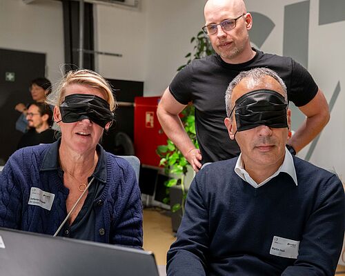 Eine Frau und ein Mann versuchen, mit verbundenen Augen am Laptop online ein Sofa zu bestellen.