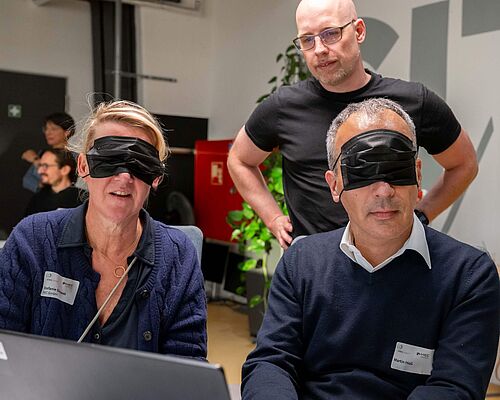 Eine Frau und ein Mann versuchen, mit verbundenen Augen am Laptop online ein Sofa zu bestellen.