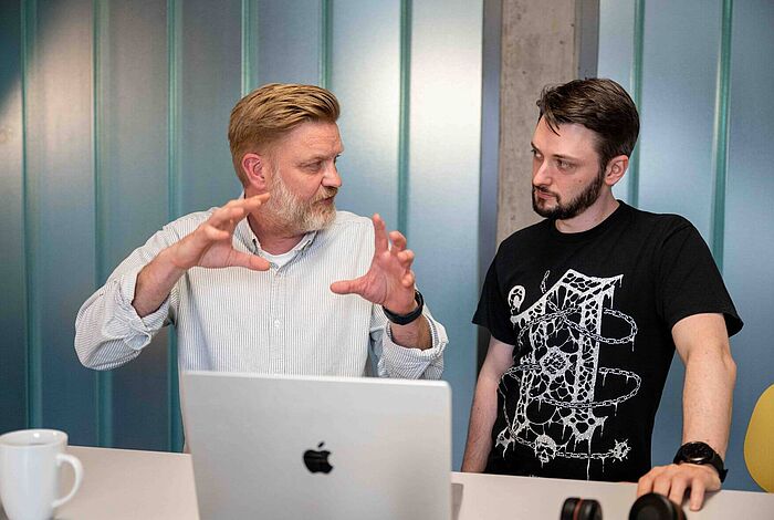 Zwei Männer sitzen vor einem Laptop und diskutieren