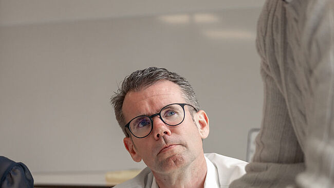 Ein Mann in einem Workshop schaut skeptisch zu einem anderen, der etwas mit Lego baut.