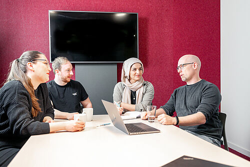 Personen diskutieren fröhlich an einem Arbeitstisch.