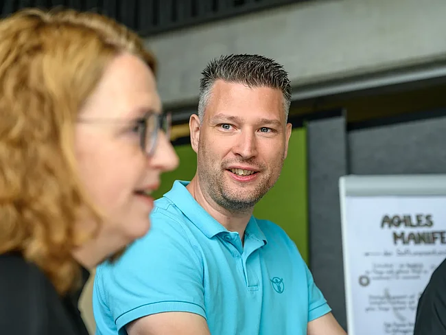 Mitarbeitende der HEC, vor einem Plakat mit dem Agilen Manifest