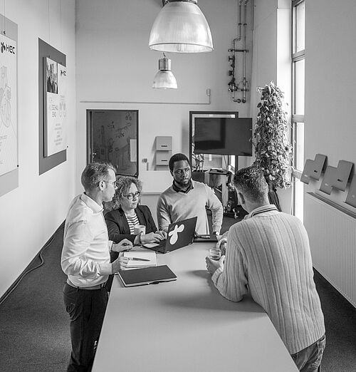 Mehrere  Menschen stehen um einen Stehtisch in einem hohen, offenen Raum im Bürogebäude