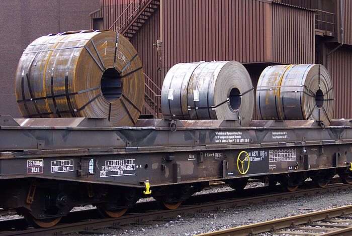 Mehrere Stahlcoils liegen auf Eisenbahn-Anhänger