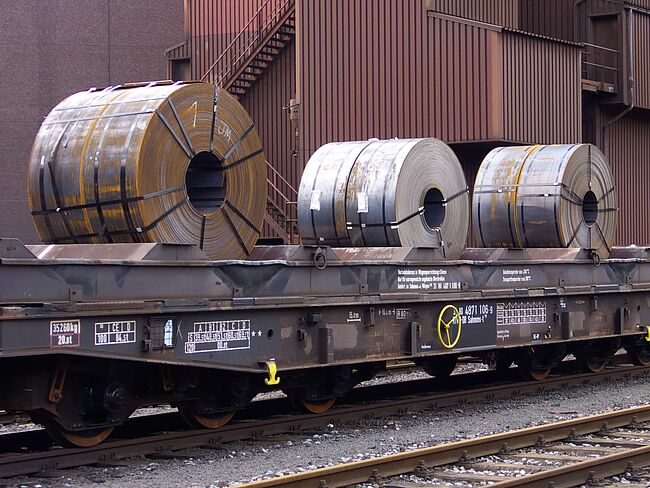 Mehrere Stahlcoils liegen auf Eisenbahn-Anhänger