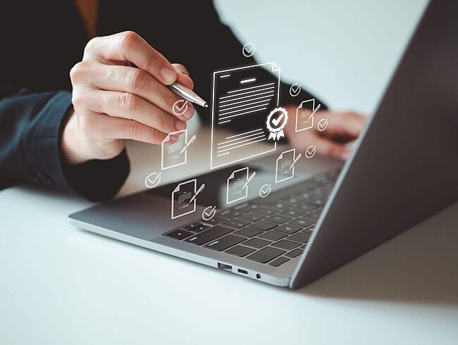 Eine Hand zeigt mit Stift auf Laptop