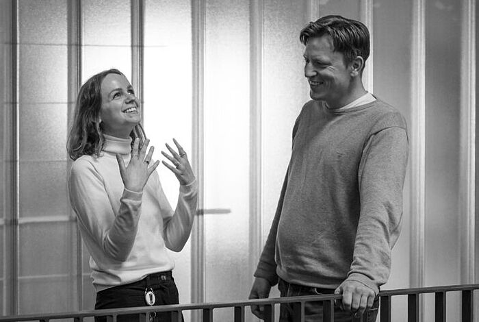 Mitarbeitende im Gespräch Ein Mann und eine Frau stehen auf einer Galerie im Foyer der HEC und sprechen angeregt mit einander.