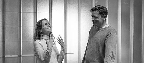 Ein Mann und eine Frau stehen auf einer Galerie im Foyer der HEC und sprechen angeregt mit einander.