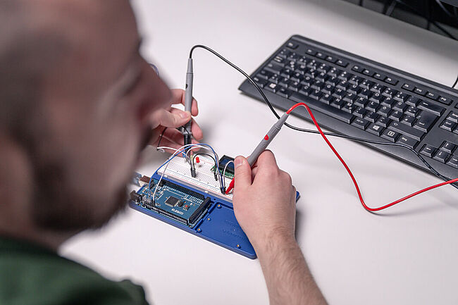 IoT-Entwickler Kevin Czesla sitzt am Schreibtisch und bearbeitet Platinen