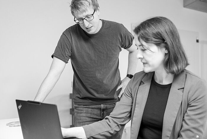 Mitarbeitende diskutieren vor Laptop Eine Frau arbeitet am Laptop und zeit einem Mann, der neben ihr steht, etwas auf dem Bildschirm.