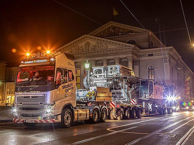 Ein Schwertransport fährt in der Nacht an einem großen, historischen Gebäude vorbei