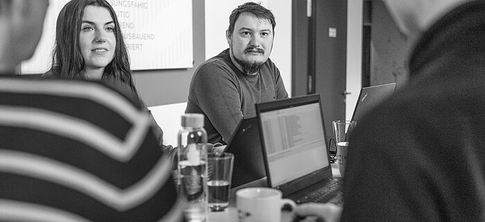 Vier Personen stehen lächelnd an einem Besprechungstisch