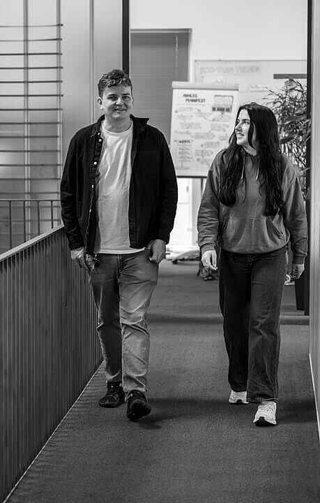 Ein Mann und eine Frau gehen auf der Galerie im Foyer der HEC im Gespräch neben einander her.